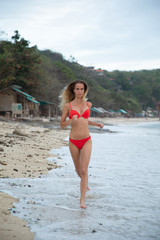 A beautiful sexy girl model relax on white sand beach, in red bikini swimsuit, with a tanned body,...