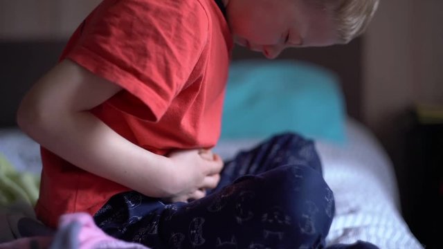 little boy is holding his hands to his stomach and writhing in pain. abdominal pain in a child.