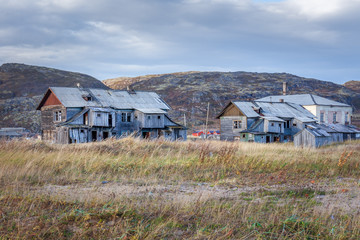 Russia, Arctic, Kola Peninsula, Barents Sea, Teriberka: Run down abandoned wooden house in the city center of the old Russian settlement small fishing village with green grass and grey cloudy sky