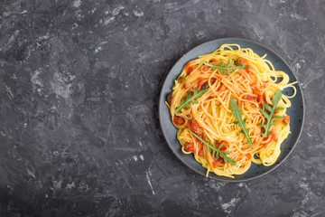 Corn noodles with tomato sauce and arugula on a black concrete background. Top view, copy space.