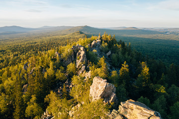 Stones of rocky Ural-Tau ridge among green forest at sunset, panoramic aerial view. Ural mountains wild nature landscape near Zlatoust, Chelyabinsk Oblast, Russia