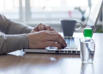 stay at home work office. Young european man taping on keyboard of laptop. Concept of quarantine home office. Sanitize and cup of hot beverage on work table