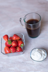 a cup of coffee and a strawberry with a transparent plate and a cream with a transparent plate