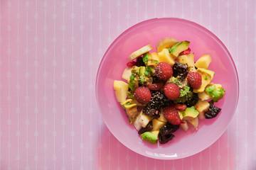 Italian breakfast with fresh fruit salad in pink bowl: avocado, raspberries, apple, banana, plums, almonds, goji berries and chia seeds