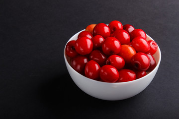 Fresh red sweet cherry in white bowl on black background. side view.