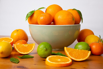 Grey ceramic bowl with fresh citrus fruits standing on wooden desk. Mandarins, limes and sliced oranges with leaves laying on table. Side view. Studio shot. Nutrition and vegetarian concept