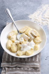 Russian and Ukrainian cuisine. Lazy dumplings with sugar, butter and sour cream in a white plate with a spoon on a light grey background. Flatlay, top view. Background image, copy space