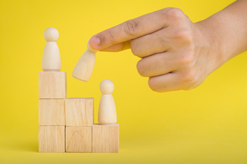 The hand is picking or select wood figure on the wooden  Stacked in human resource management concepts Teamwork.Success Leadership,Business Progress and Competition on yellow backgrond and copy space.