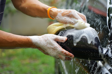 Hand of man holding sponge  and foam washing car closedup image