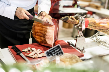 Salumiere toglie via il grasso con un coltello da una coscia di prosciutto crudo nel banco della sua salumenria