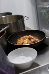 tegame con della carne in cottura in mezzo ad altre pentole nei fornelli di una cucina