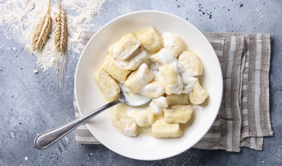 Russian and Ukrainian cuisine. Lazy dumplings with sugar, butter and sour cream in a white plate with a spoon on a light grey background. Flatlay, top view. Background image, copy space
