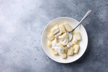Russian and Ukrainian cuisine. Lazy dumplings with sugar, butter and sour cream in a white plate with a spoon on a light grey background. Flatlay, top view. Background image, copy space