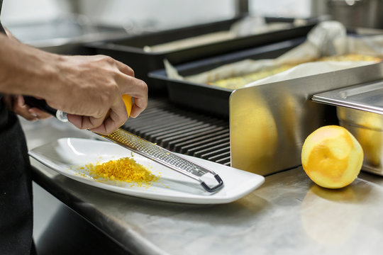Cuoco grattugia la buccia del limone in un piatto bianco in cucina