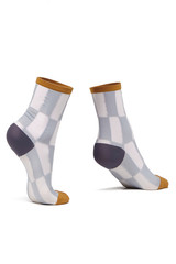 Cropped shot of female feet on tiptoe in thin socks with black and white chessboard pattern, mustard toes and rims and gray heels. The photo is made on the white background.  