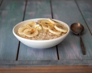 Milk oatmeal with banana and cinnamon in a deep plate and spoon on a wooden background