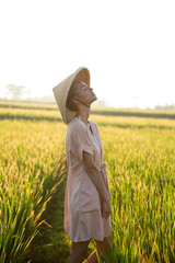 Beautiful girl in a rural hat collects rice from the field, view of the province of Asia. Model with blond hair works in the rice field in dress. Clean nature, healthy ecology, agritourism on Bali.
