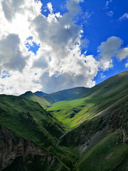 View of the Alpine mountains with a deep gorge and a river. Around green meadows and rocks. Mountains of the North Caucasus in the summer.