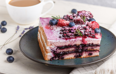 Berry cake with milk cream and blueberry jam on blue ceramic plate with cup of coffee and fresh blueberries on a white wooden background. side view, selective focus.