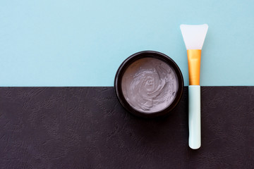 Opened jar of grey clay mud mask for face and body on mint and black background with soft brush behind.Homemade skincare organic product for face skin care and treatment.Flat lay, top view.