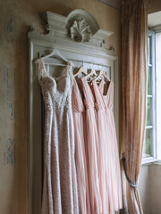A white wedding dress and bridesmaids dresses in pink are hanging on an old vintage wardrobe of light green color.