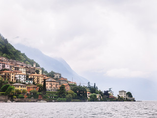 Italy. Lake Como. Green high mountains in the clouds with small houses and villages in red, yellow and white colors. down below is Lake Como. Overcast