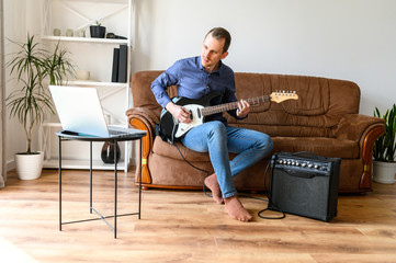 Online studying, webinars. A young man is shows how to play electric guitar to laptop webcam