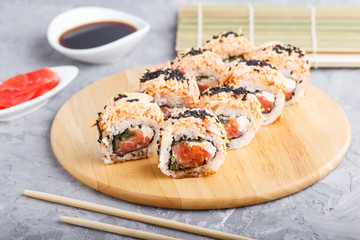 Japanese maki sushi rolls with salmon, sesame, on wooden board on a gray concrete background. Side view