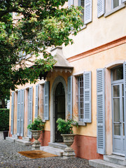 Entrance to a beautiful yellow Italian villa with windows with gray shutters, decorated with flowerpots with greenery and pebbles on the floor