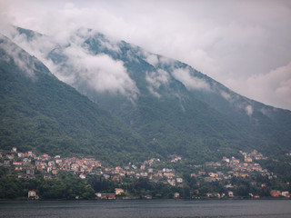 Italy. Lake Como. Green high mountains in the clouds with small houses and villages in red, yellow, and white colors. down below is Lake Como. Overcast
