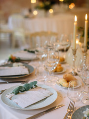Served beautiful table, three glasses, plates with eucalyptus, breakfast bread, candles and a bouquet