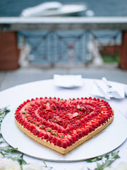 Red creamy heart cake decorated with whole strawberries., On a white table. overlooking the yacht and the sea on the wedding Italy party