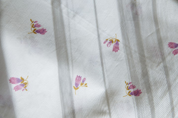 white fabric bedding folds print purple flower and shade from the curtains