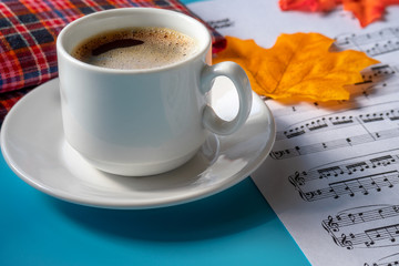 morning music composition. music notes and a cup of strong coffee on a blue background. autumn leaves on a sheet of paper with musical notes