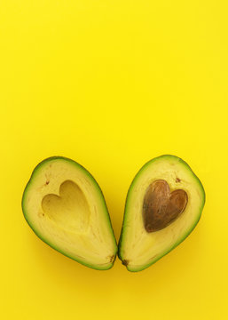 Flat lay of cut in half avocado with seed in shape of heart on yellow background love forever inseparable concept