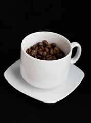 A white Cup and saucer with black coffee beans stands on a black table