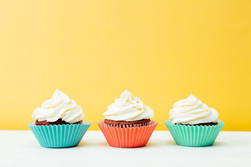 Three colorful  cupcakes on a yellow background
