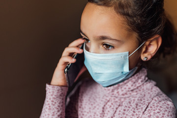 Young girl wearing a mask to prevent the virus speaks on a mobile phone.