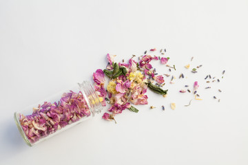 Opened glass bottle with dry mix of flowers on white background