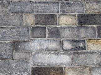 a full frame image of a large old dark stone wall made of large irregular sandstone blocks
