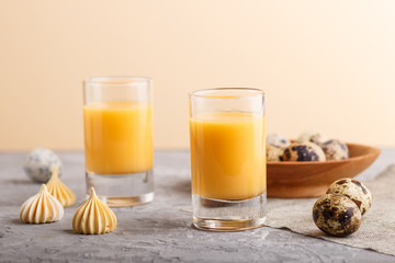 Sweet egg liqueur in glass with quail eggs and meringues on a gray and orange background. Side view