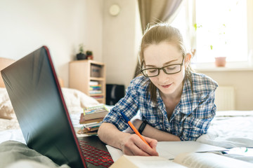 Student is passing online lesson on the Internet at home lying on a bed. Remote learning in schools and universities