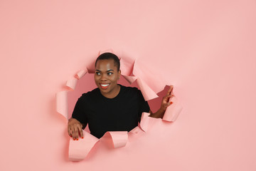 Smiling. Cheerful african-american young woman poses in torn coral paper background, emotional and expressive. Breaking on, breakthrought. Concept of human emotions, facial expression, sales, ad.