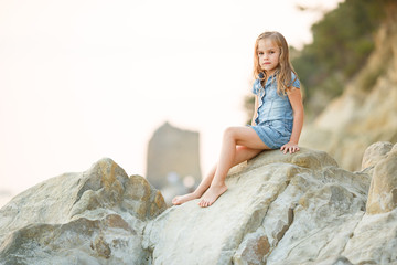 little girl sitting on rock at sunset. travel.