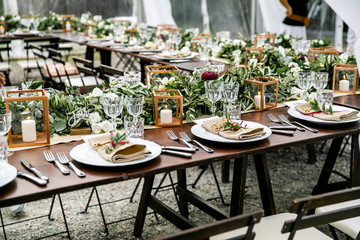in backyard of villa in Tuscany there is banquet wooden table decorated with cotton and eucalyptus compositions, glasses, candles and plates are placed on table