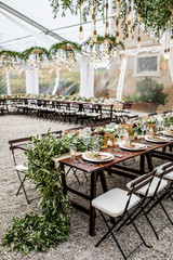 in backyard of villa in Tuscany there is banquet wooden table decorated with cotton and eucalyptus compositions, glasses, candles and plates are placed on table