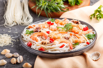 Rice noodles with shrimps or prawns and small octopuses on gray ceramic plate on a black concrete background. side view, close up.
