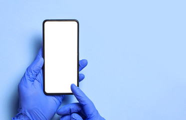 Male hands in blue medical gloves hold smartphone with white blank screen on blue background. Protecting Health During a Pandemic coronavirus 2019-nCoV Hands medical worker volunteer doctor with phone