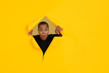 Wondered. Cheerful african-american young woman poses in torn yellow paper background, emotional...