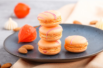 Orange macarons or macaroons cakes on blue ceramic plate on a gray concrete background. side view, selective focus.